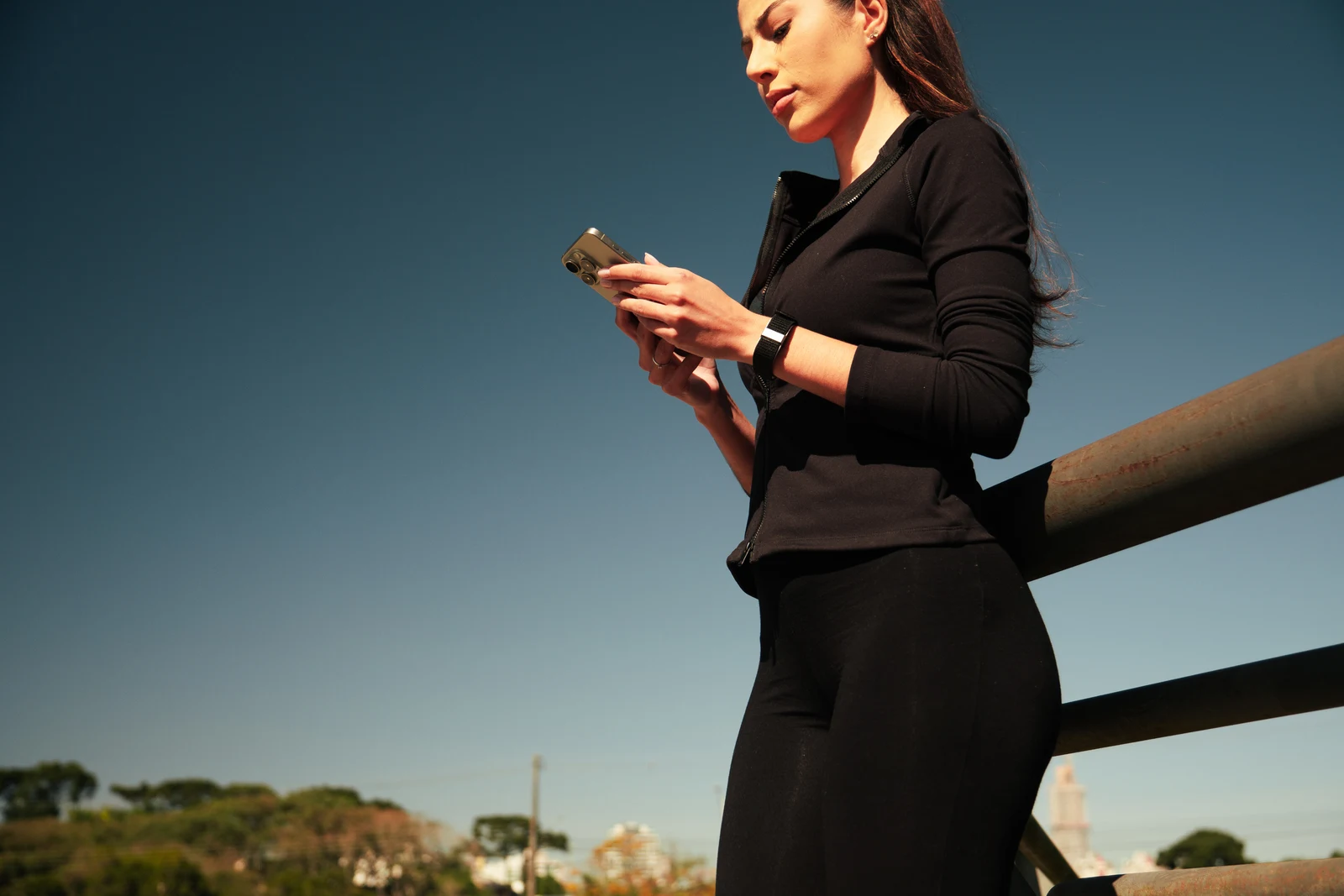 Mulher usando a pulseira enquanto consulta o celular ao ar livre